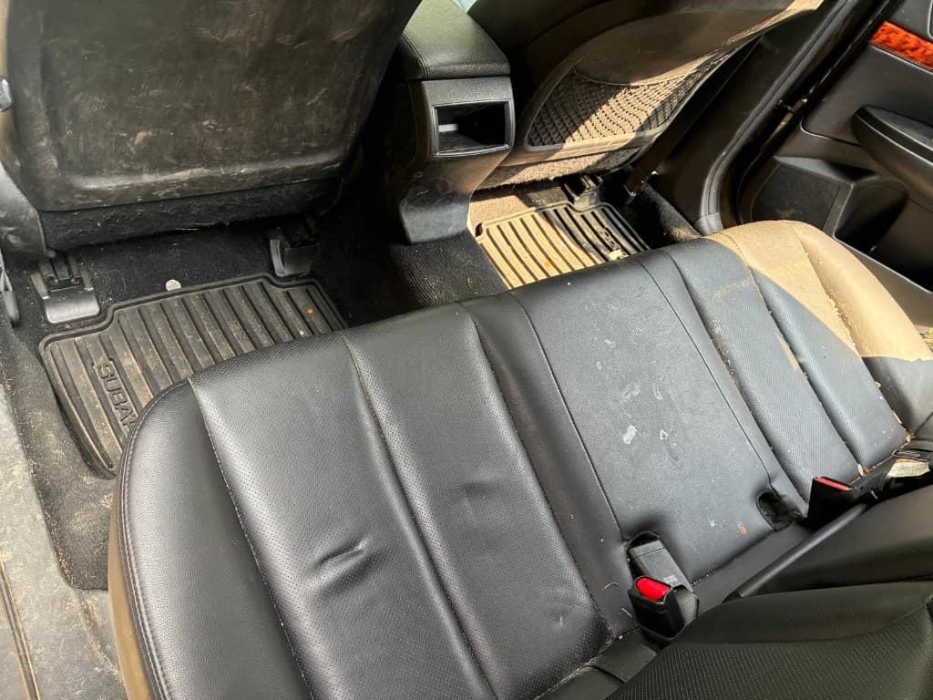 Dirty rear seats and floor mats covered in crumbs and mud before interior detailing
